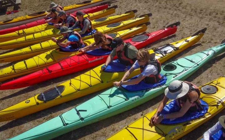 a group of students sit in beached kayaks while preparing for their expedition 